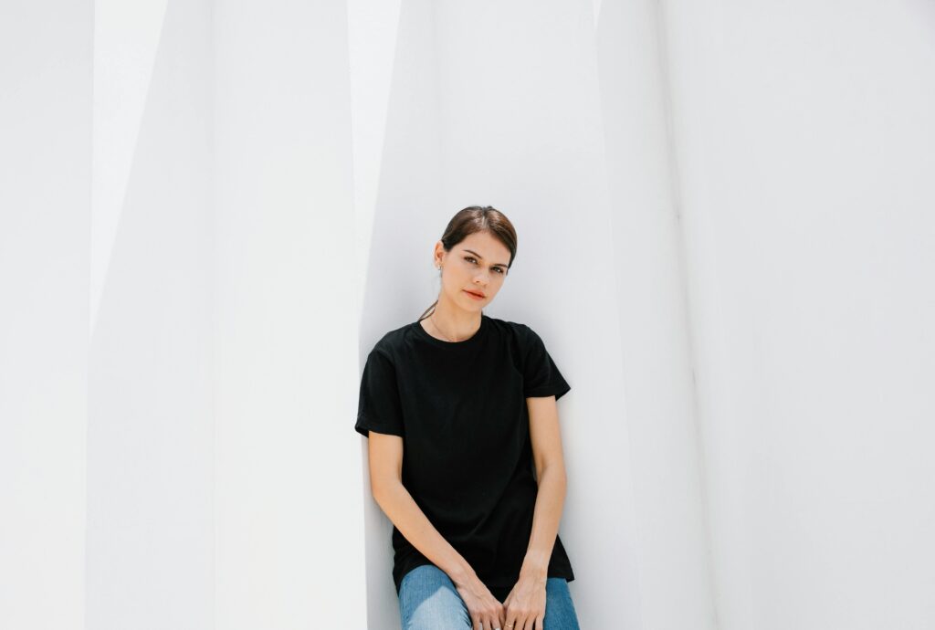 Young gentle female model in casual outfit looking at camera against ribbed wall in sunshine